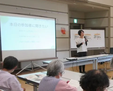 公民館でのセミナー。スクリーンの前で話す片付けい子と、席につく参加者